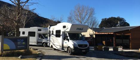 A travel trailer with 'maui' branding parked in front of a building with a sign reading 'TOP Holiday Parks Queenstown'.