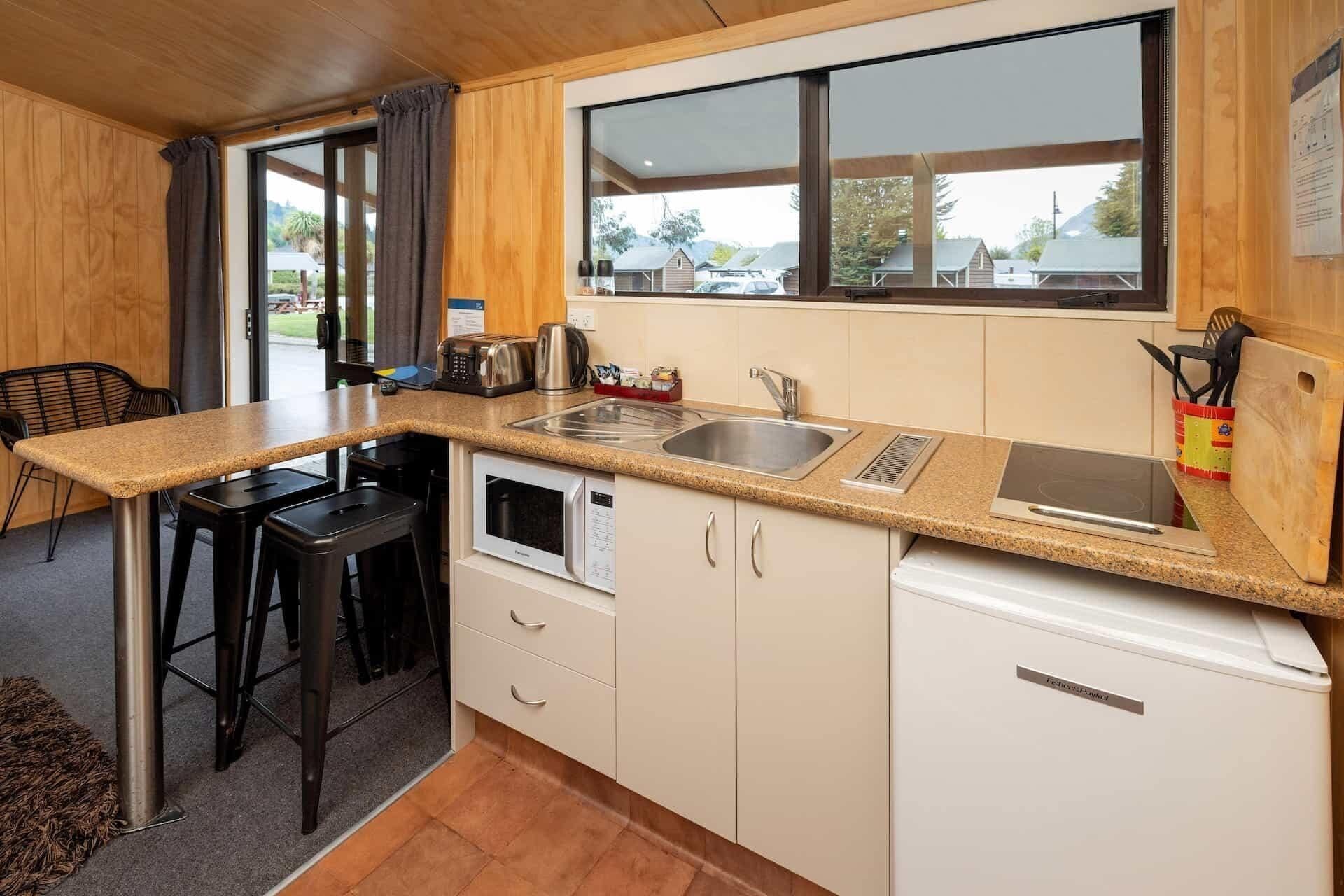 A compact kitchen with a microwave, sink, and a small refrigerator. There is a window providing a view of the outside.