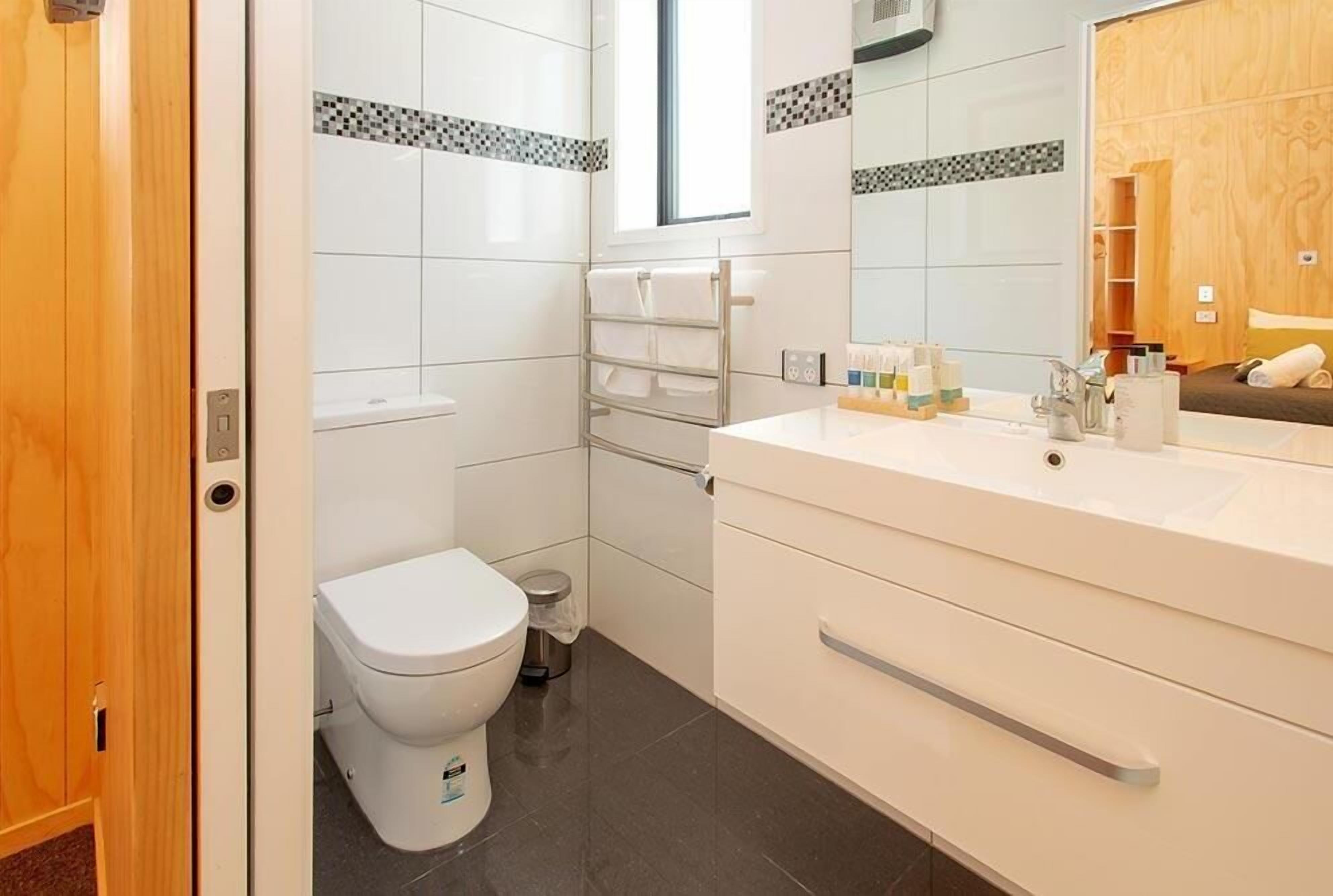 Et moderne badeværelse med et hvidt toilet, en vask med spejl og en bøjle til håndklæder.