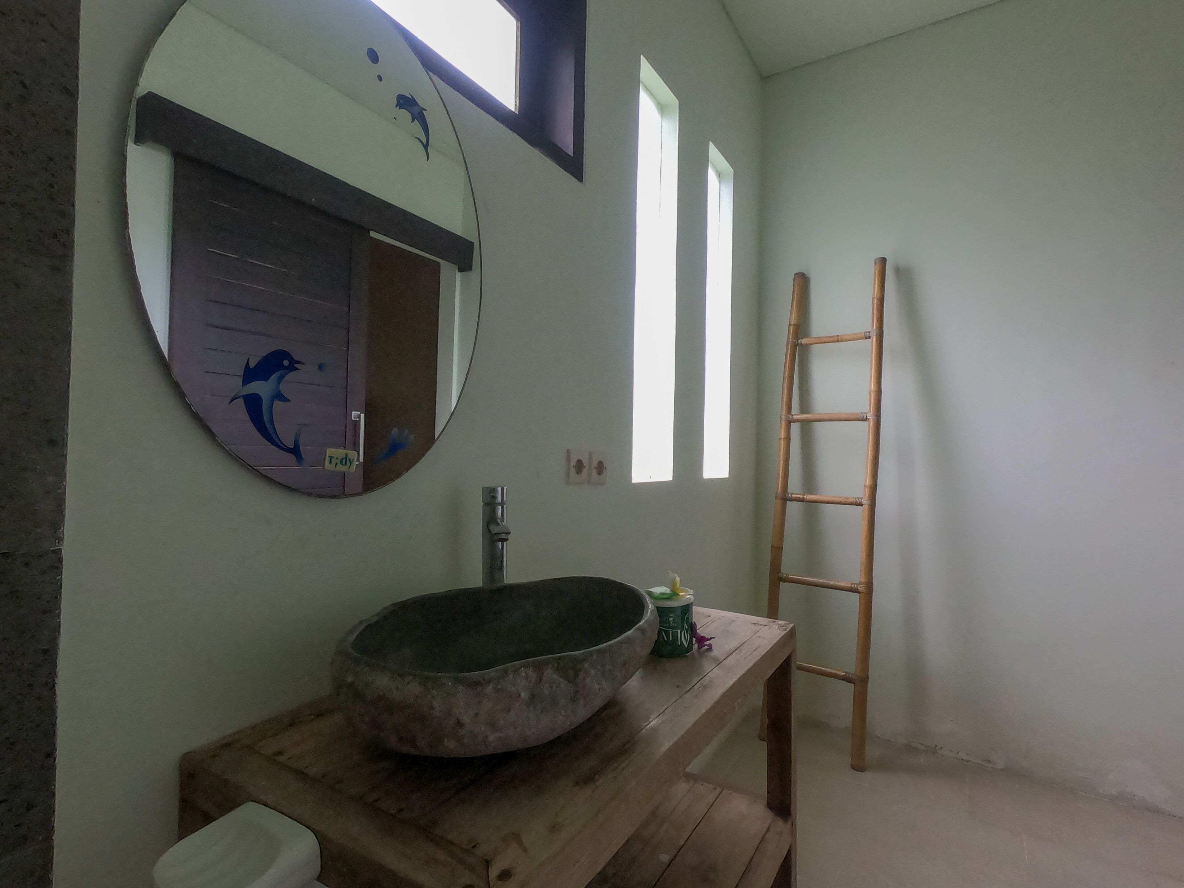 Un baño con un espejo redondo, un lavabo de piedra, un banco de madera y una escalera.