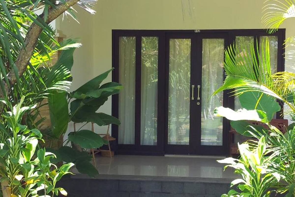 A building with a large glass door and windows, surrounded by lush greenery.