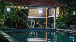 A swimming pool with a tiled deck, surrounded by tropical plants and a covered seating area. - Medori Putih Homestay (Pecatu)