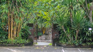 A paved pathway leading to a stone archway surrounded by dense foliage. - Medori Putih Homestay (Pecatu)
