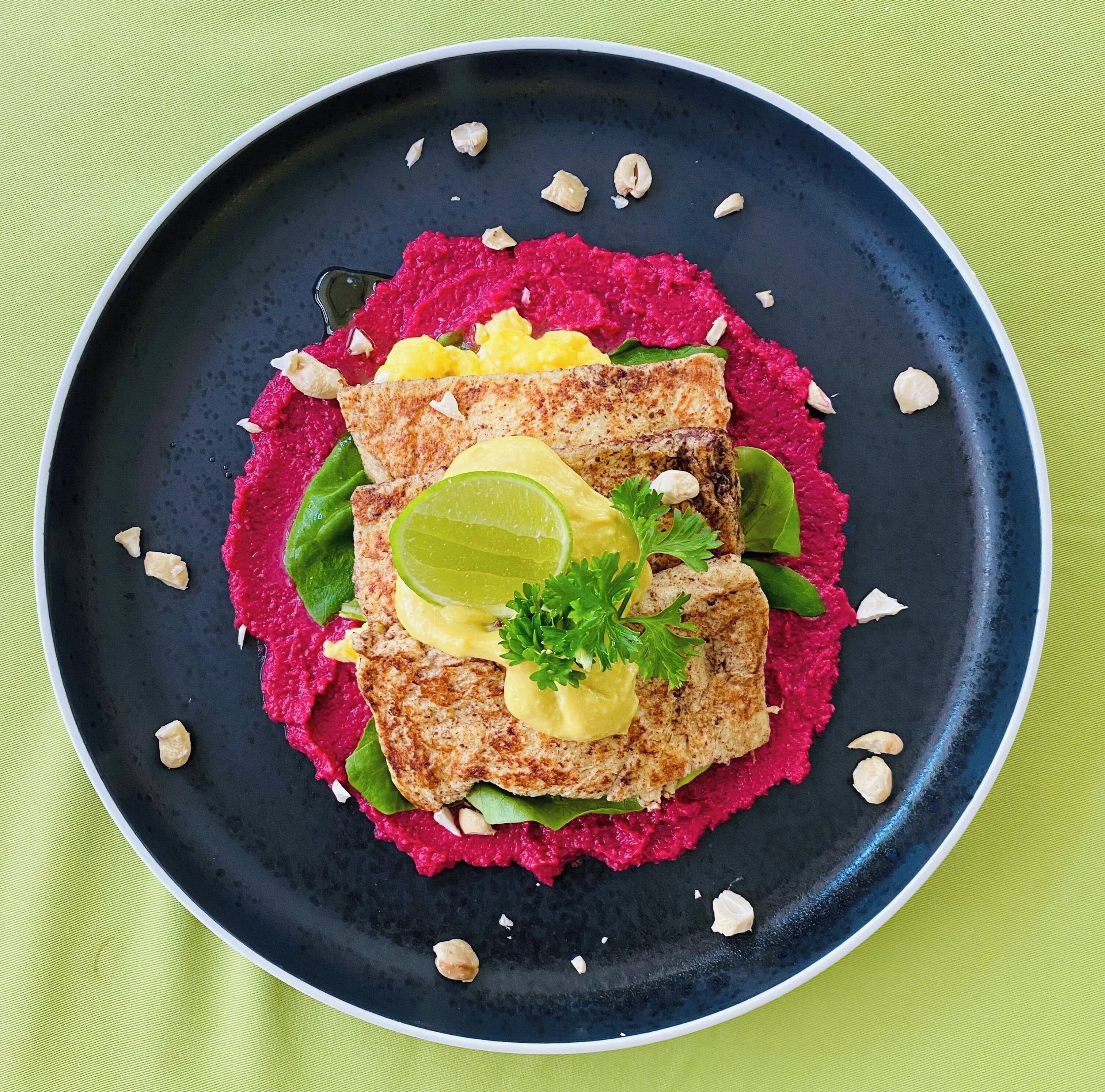 Egy sötétkék szélű tányér, melyen grillezett halfilé, egy szelet avokádó, egy limekarika és egy csipetnyi petrezselyem található, mindez pedig egy rétegnyi céklapürén van elrendezve.