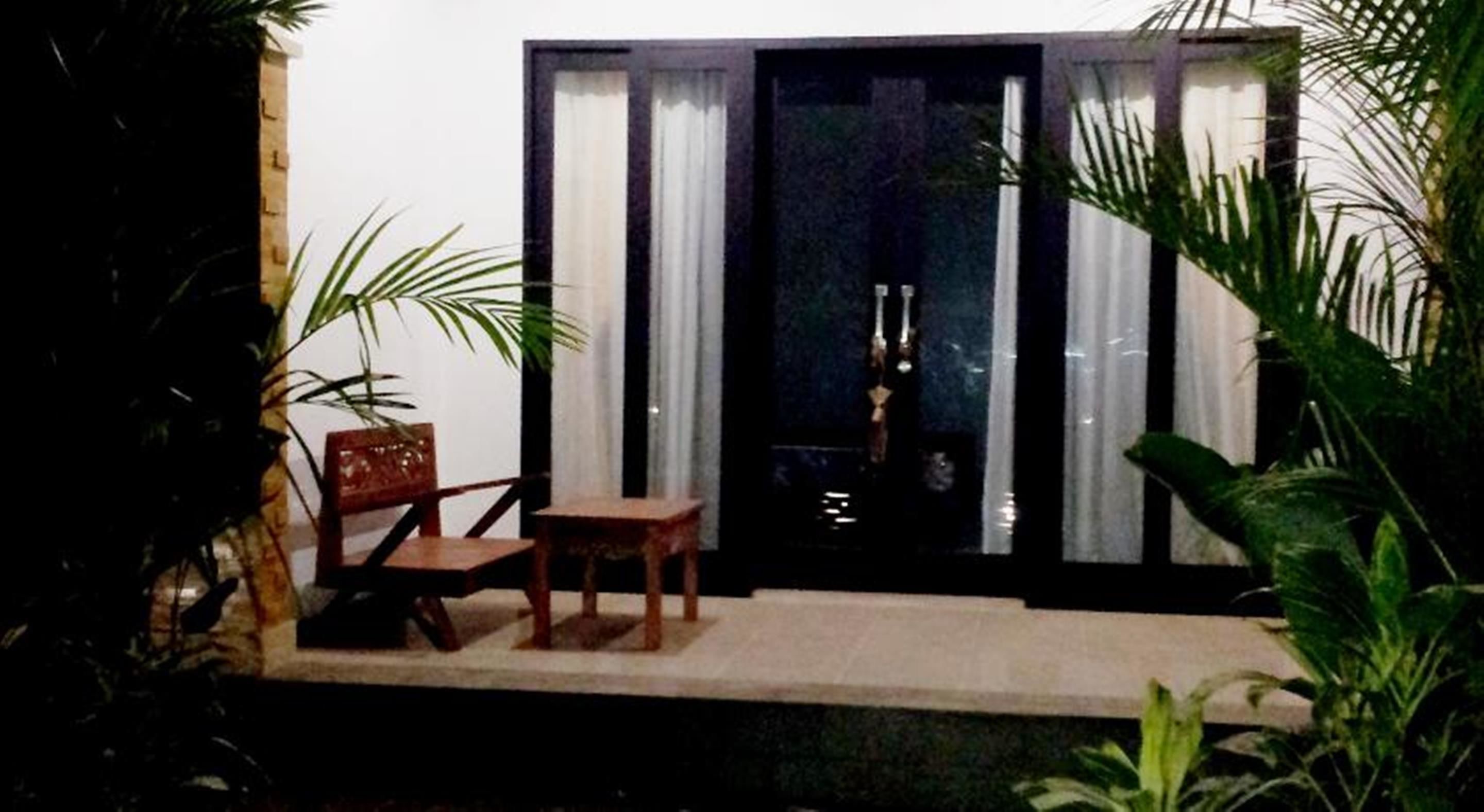 Un pequeño espacio al aire libre con dos sillas de madera y una mesa, rodeado de plantas en macetas.