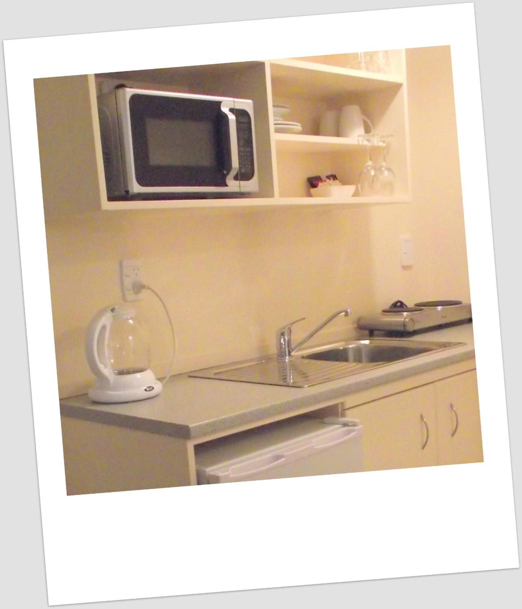 A compact kitchenette with a microwave, sink, and a kettle.