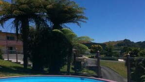 Une piscine avec un ciel bleu dégagé et un grand arbre en arrière-plan.