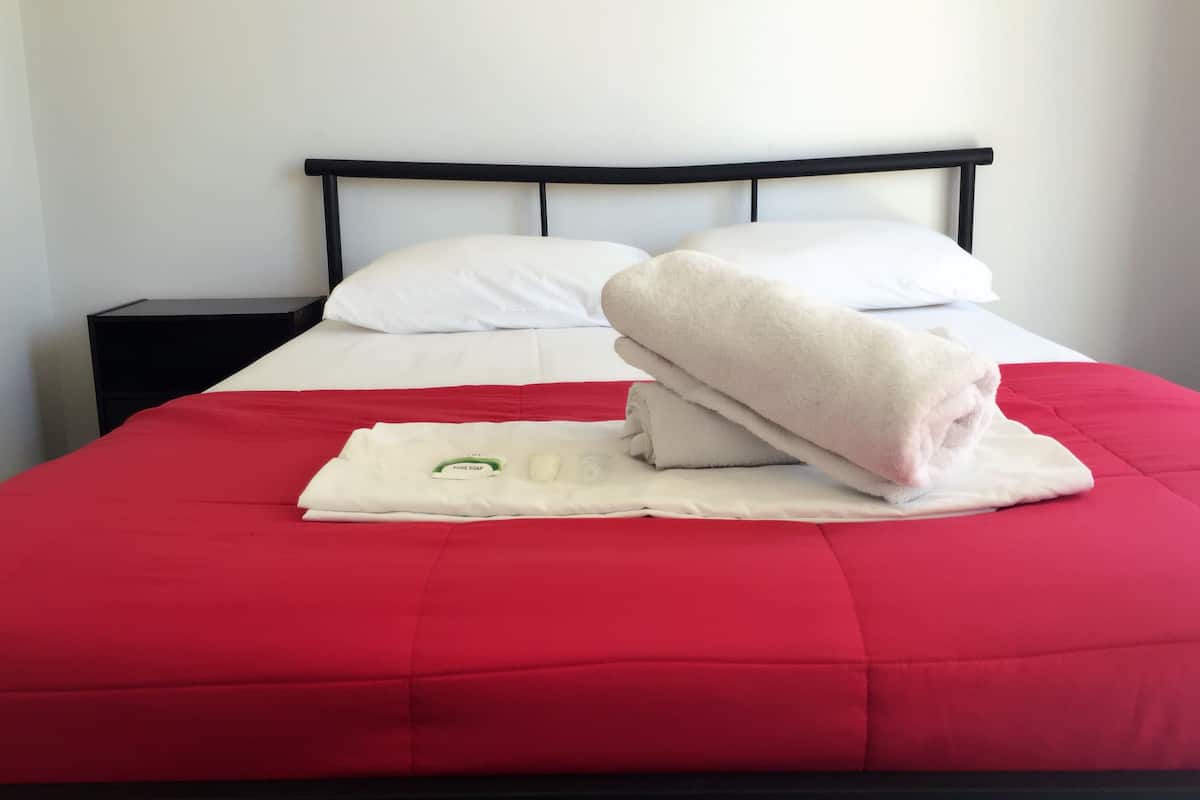 A neatly made bed with a red bedspread, white pillows, and a folded towel on top.