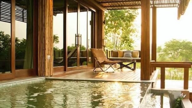 A pool area with a wooden deck, a lounge chair, and a table with cushions. - Mountain Creek Golf Resort & Residences (Sikhio)