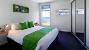 Une chambre d’hôtel avec un lit, une table de chevet, une lampe, une fenêtre donnant sur la plage et une porte coulissante.