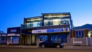 Un bâtiment moderne à la structure à deux étages, comprenant un commerce au rez-de-chaussée avec une enseigne indiquant « Tatts » et « Penguin Newsagency & Tattslotto ».