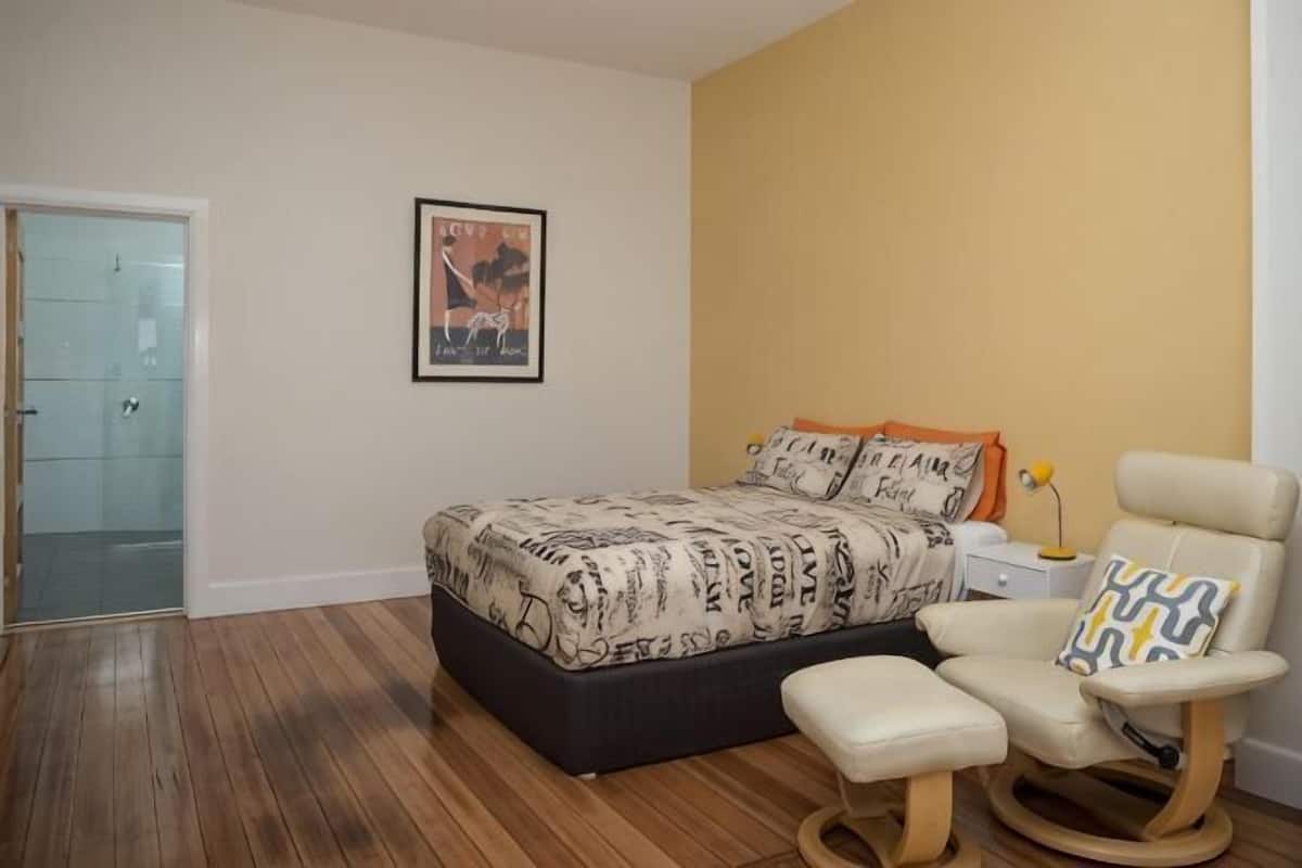 A bedroom with a bed, a chair, a bedside table, and a door.