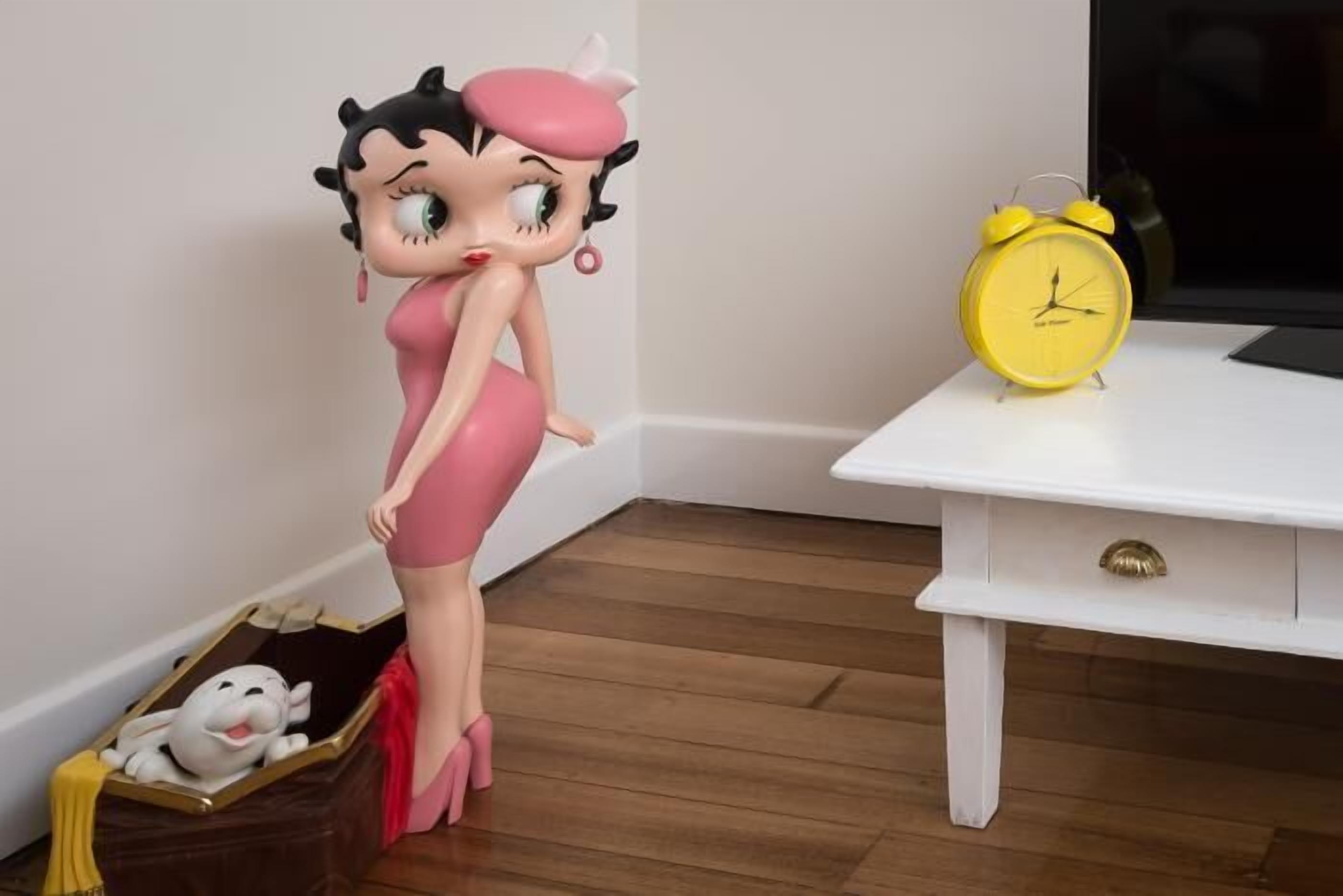 Iemand in een roze jurk staat naast een gele wekkerklok op een witte tafel.