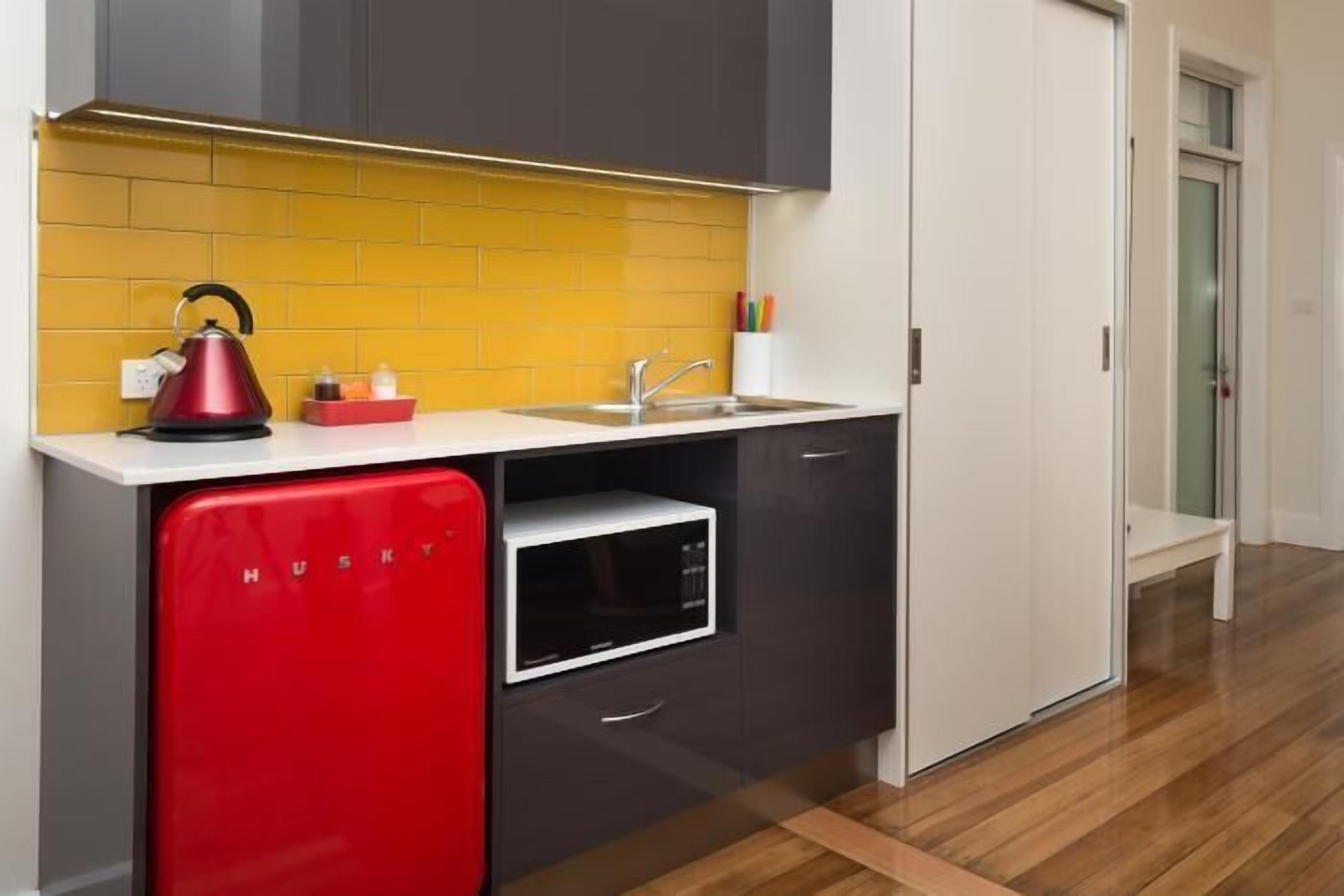 A compact kitchen with a yellow backsplash, a red appliance, and a microwave.