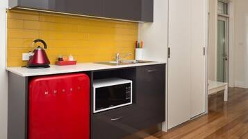 A compact kitchen with a yellow backsplash, a red appliance, and a microwave.