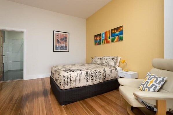 A bedroom with a bed, a chair, a nightstand, and a painting on the wall. - Penguin Waterfront Escape (Penguin)