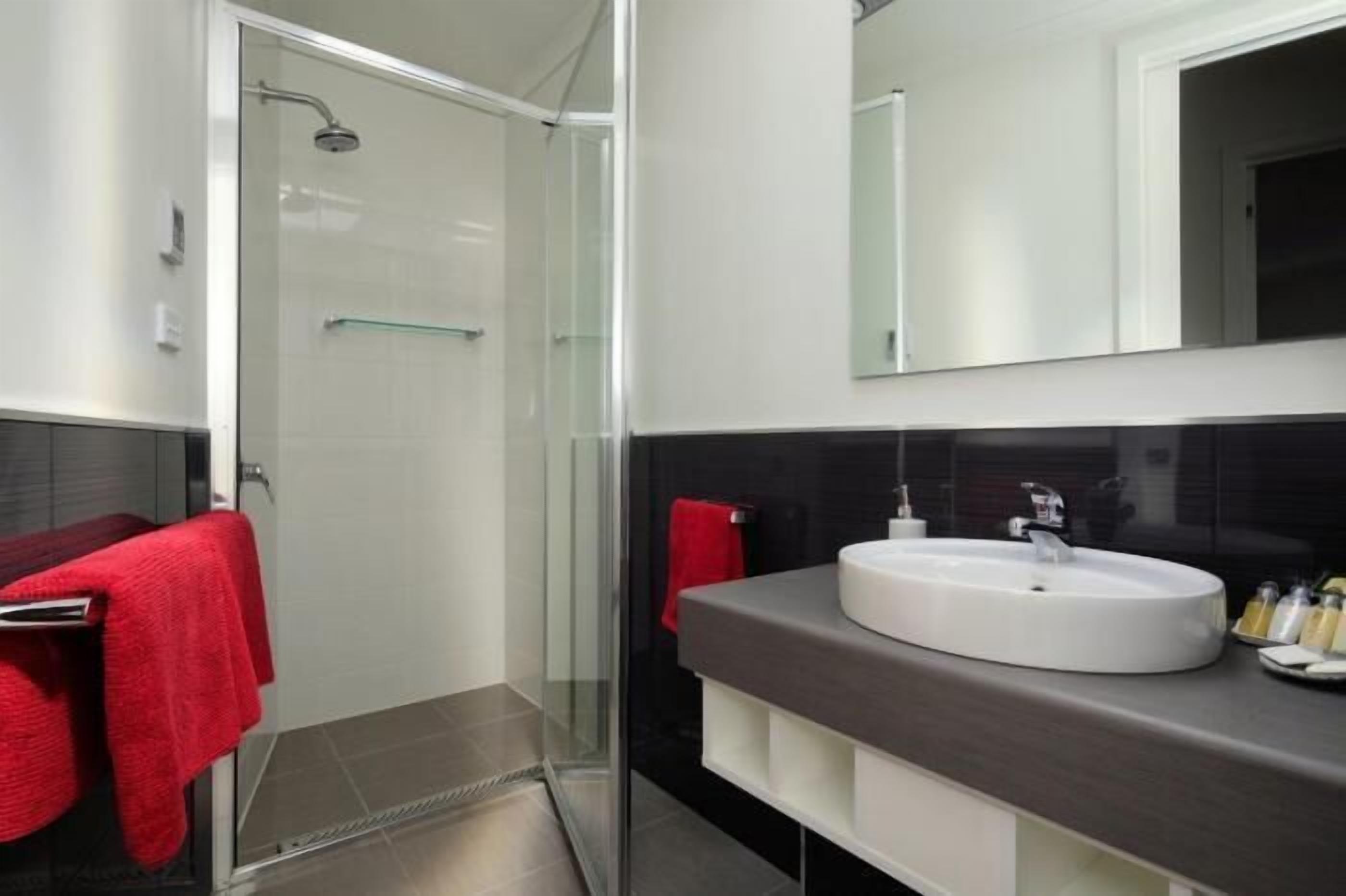 A modern bathroom with a glass shower enclosure, a white sink, and a dark countertop.