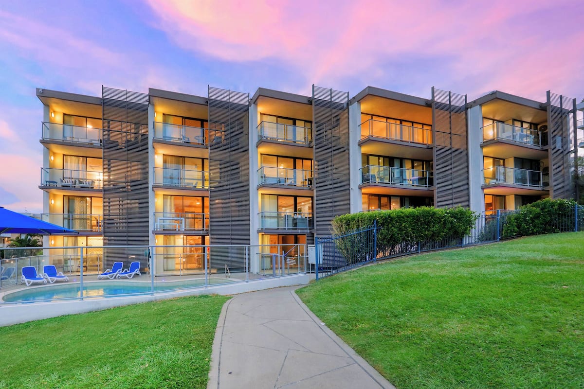 A multi-story hotel with balconies, a swimming pool, and a well-maintained lawn.