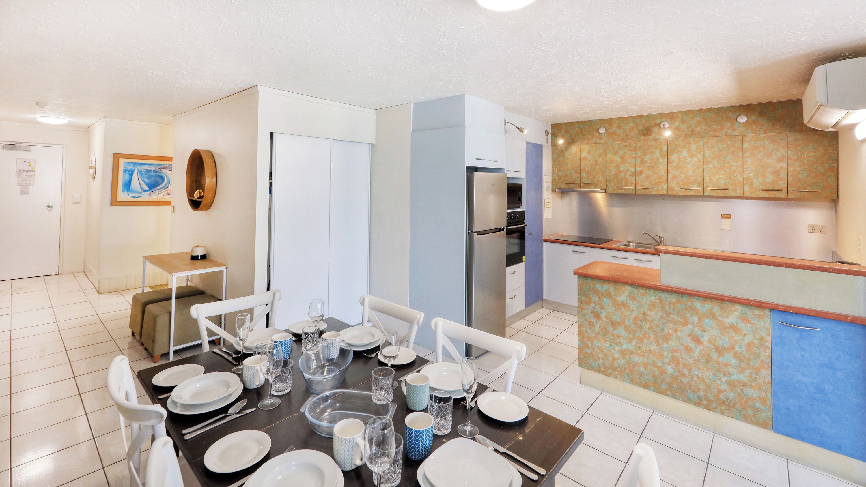 A modern kitchen with stainless steel appliances, a dining area with a table set for four, and a small kitchenette.