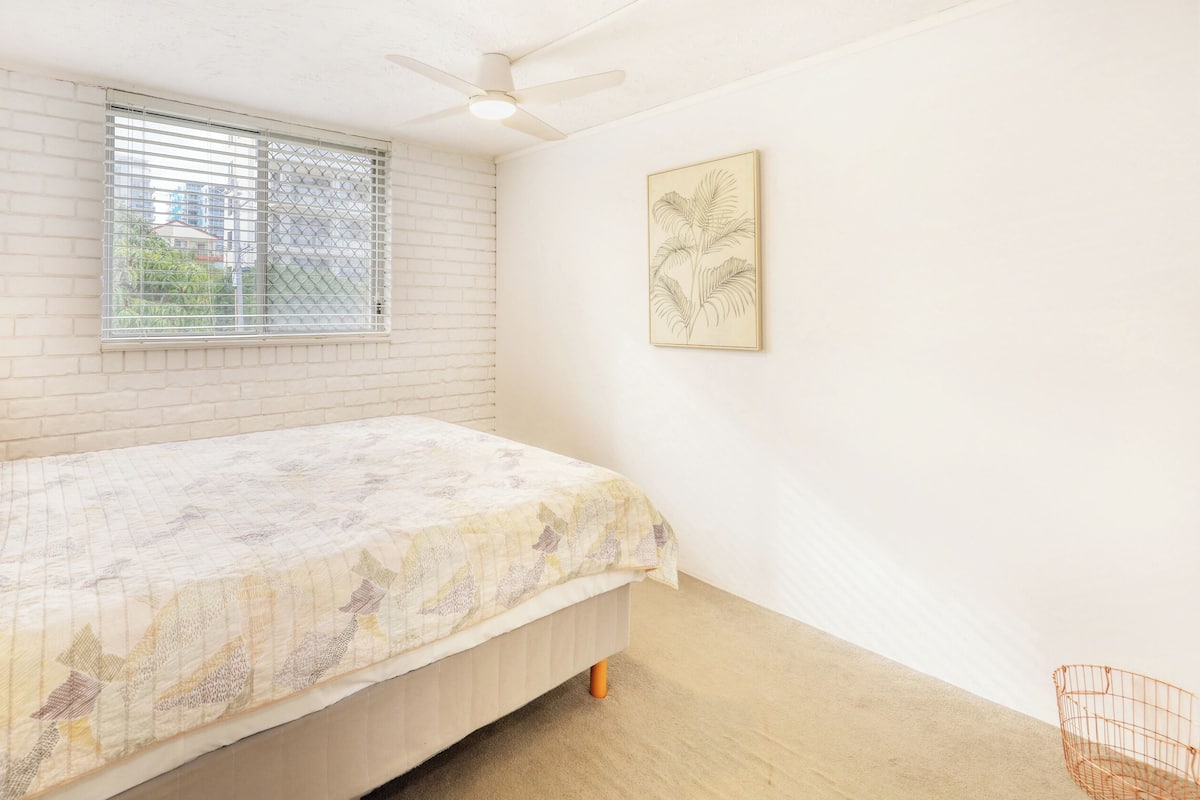 A bedroom with a bed, a window with blinds, a ceiling fan, and a wall-mounted picture.