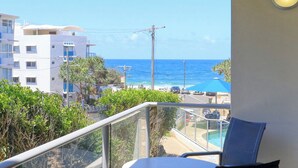 A balcony with a view of the ocean, a pool, and adjacent buildings. - Merrima Court Holidays (Kings Beach)