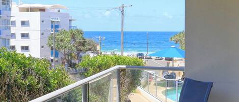 A balcony with a view of the ocean, a pool, and adjacent buildings.