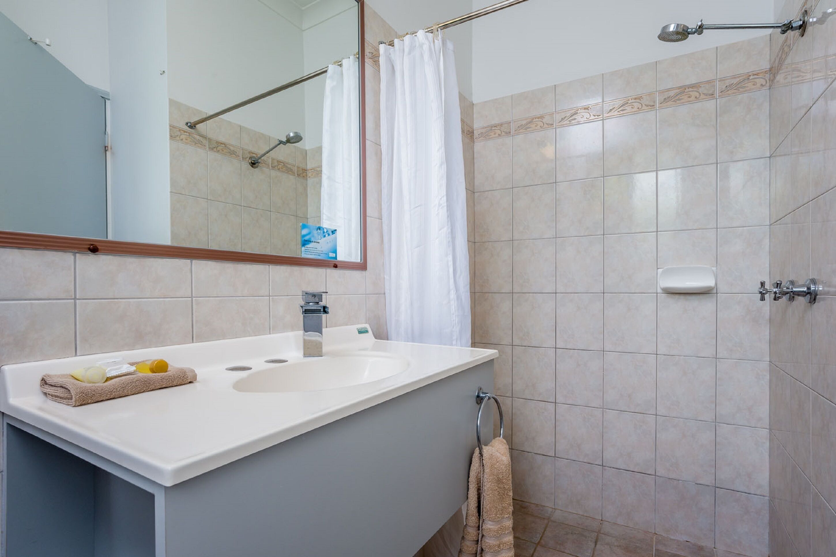 A bathroom with a large sink, mirror, shower, and towel rack.