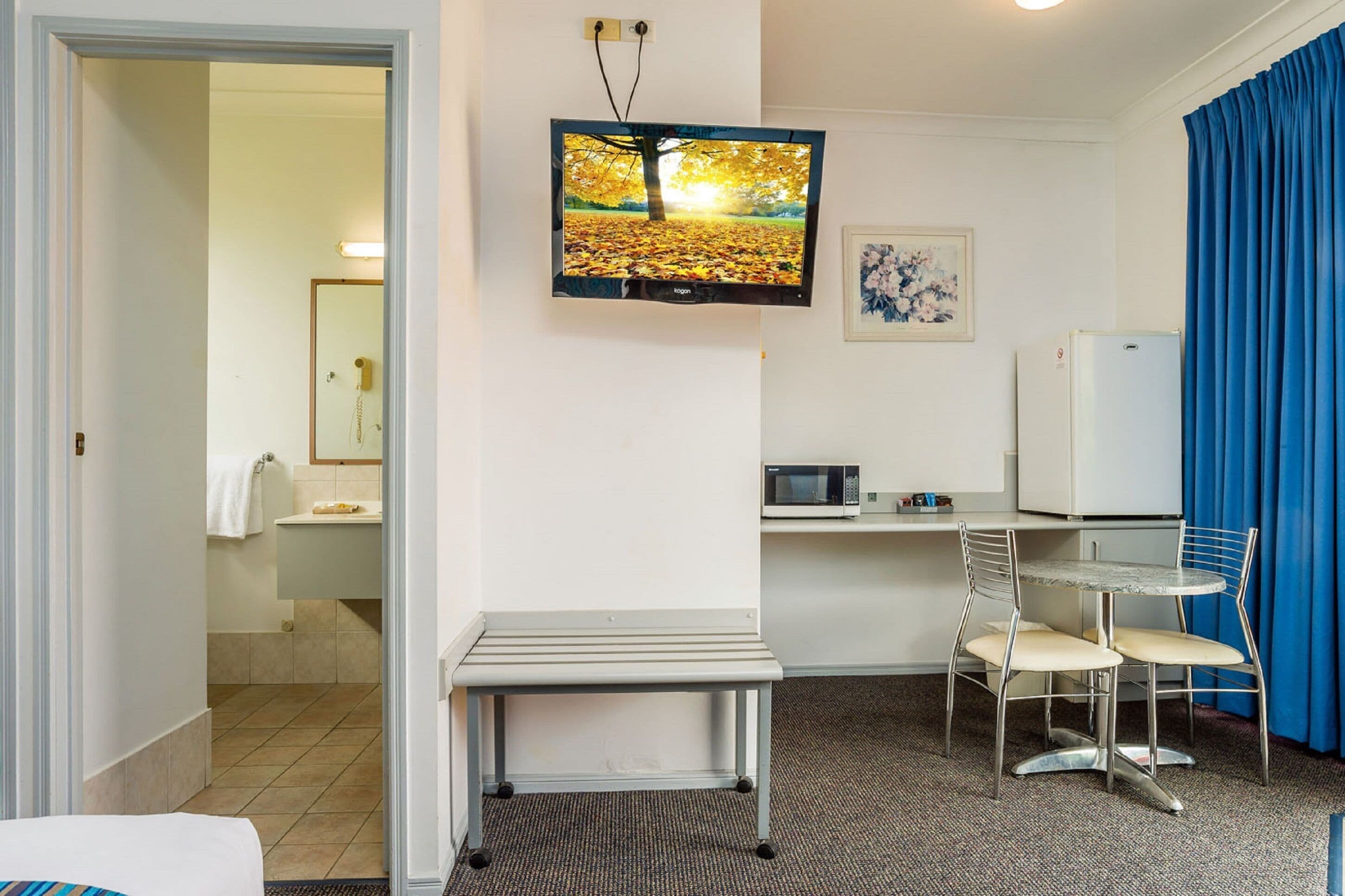 Habitació d'hotel amb un llit, una taula de treball amb una cadira, una televisió, un microones i un frigorífic.