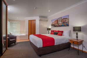 Een hotelkamer met een groot bed, een zithoek met een fauteuil, een raam met zonwering, een airconditioning en een schilderij aan de muur.