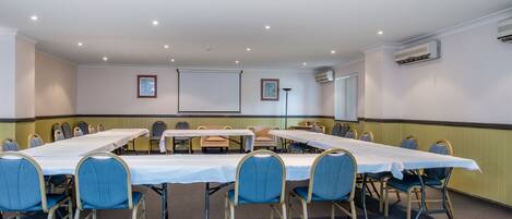 Una sala de conferencias con una larga mesa, sillas azules y una pantalla para proyector.