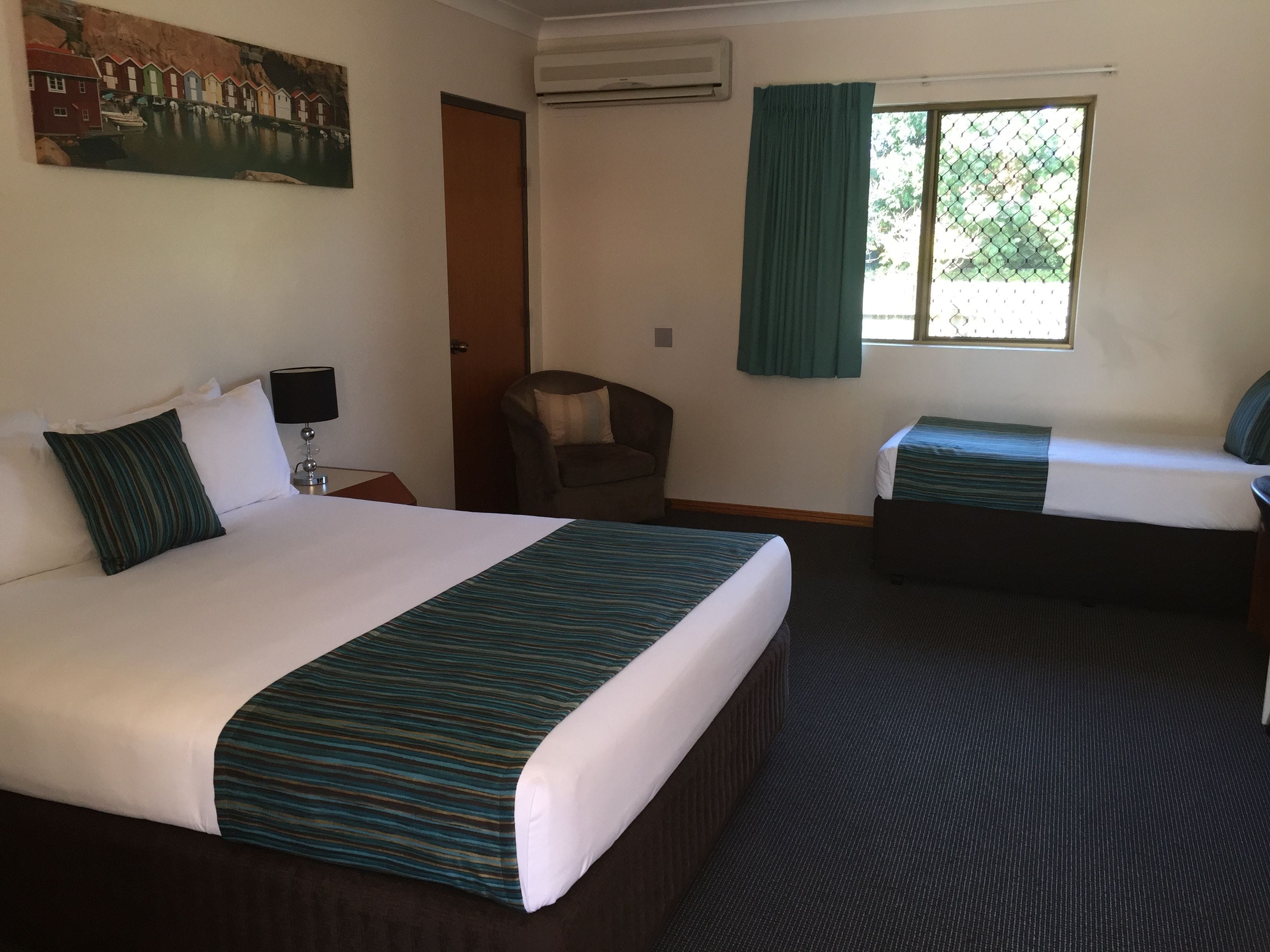 A hotel room with two beds, a chair, a painting, and a window with curtains.