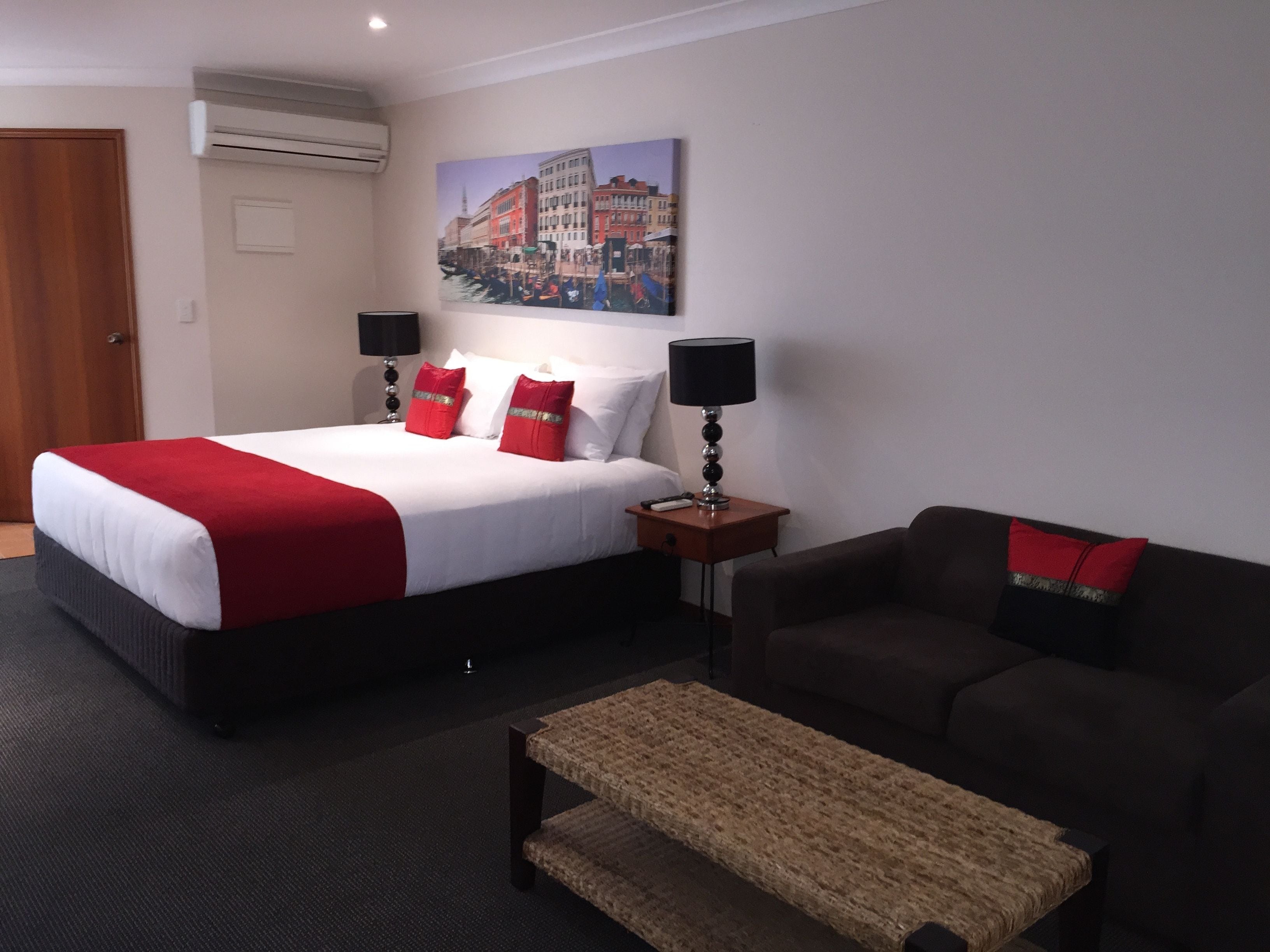 Una habitación de hotel con una cama, un sofá, una mesita y un cuadro en la pared.