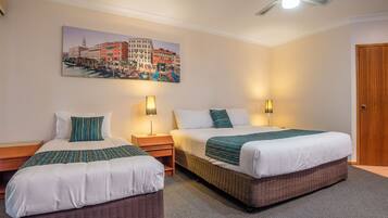 A hotel room with two beds, a ceiling fan, and a painting of Venice on the wall.