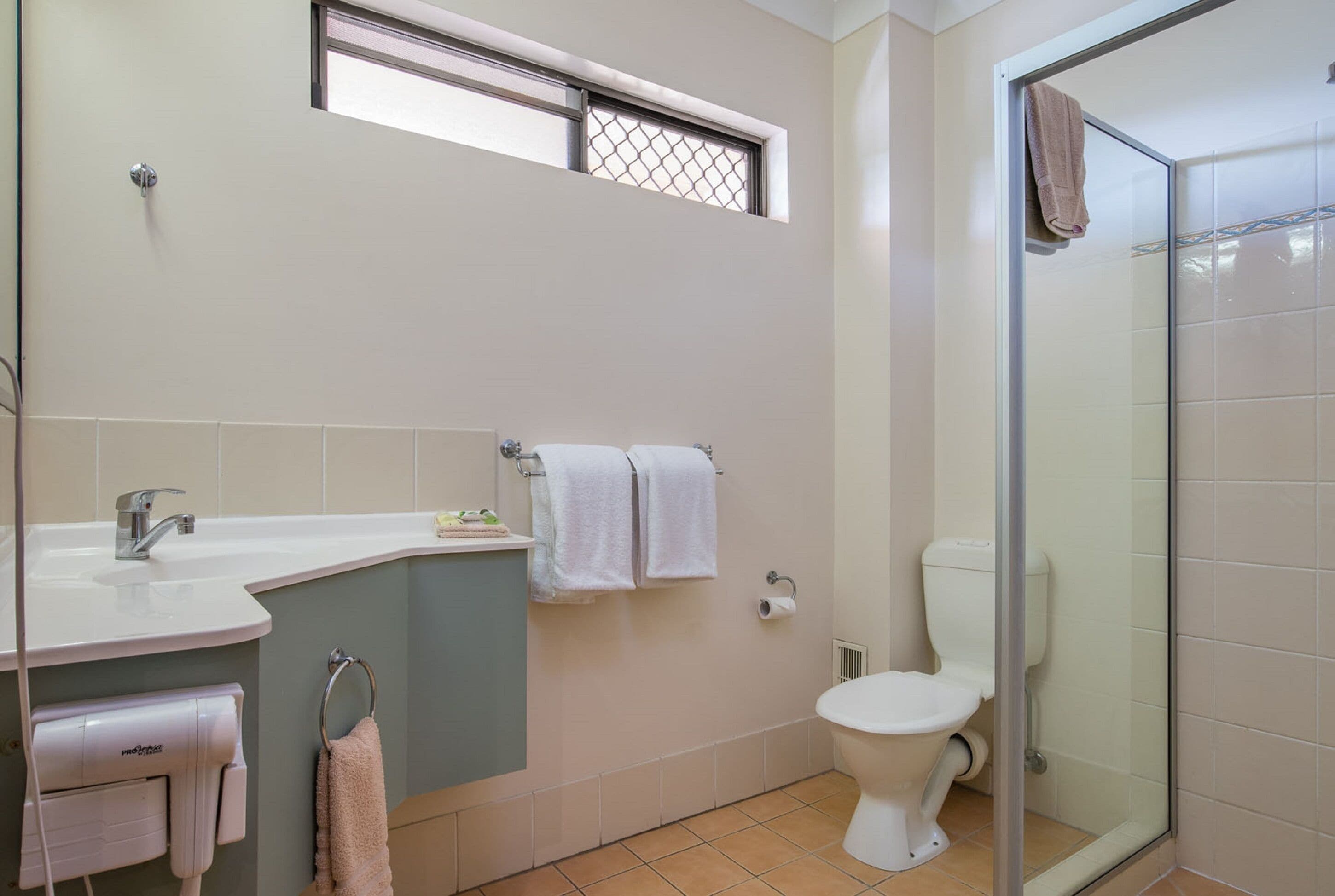 Un baño con lavamanos, dos toallas, inodoro y cabina de ducha de vidrio.