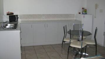 Cocina compacta con lavamanos, microondas y armarios, una mesa de comedor con sillas, y un reloj en la pared.
