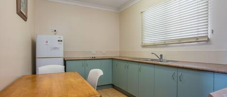 A kitchen with teal cabinets, a wooden table, a white refrigerator, and a window with blinds.