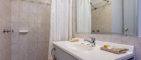 Un baño con un lavamanos blanco, dos toalleros, un espejo y una zona de ducha.