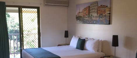 A hotel room with two beds, a ceiling fan, an air conditioning unit, a painting of a cityscape, and a sliding glass door leading to an outdoor area.