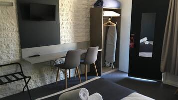 Habitación de hotel con cama, dos sillas, televisión montada en una pared de ladrillo, armario y una toalla en el suelo.
