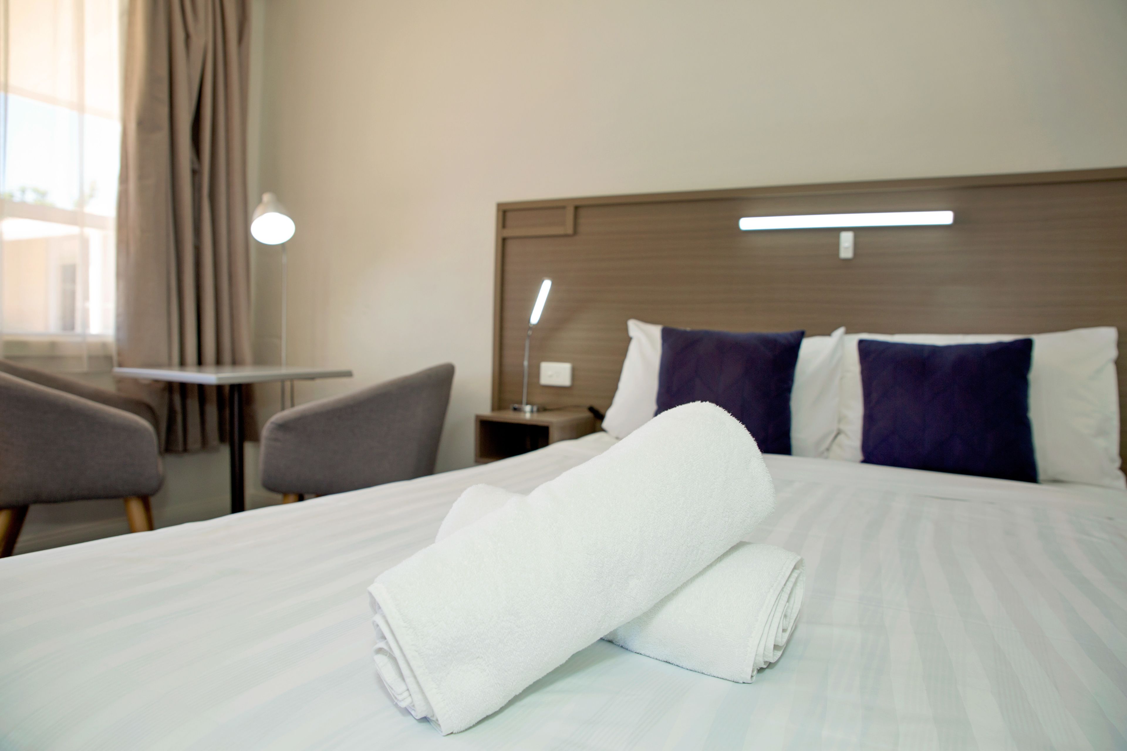 A hotel room with a neatly made bed, a bedside table, a lamp, and a chair.