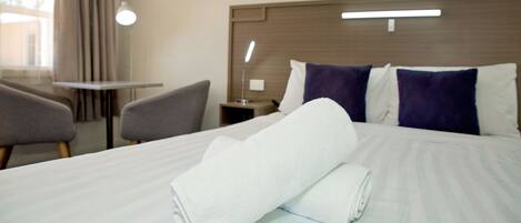 A hotel room with a neatly made bed, a bedside table, a lamp, and a chair.