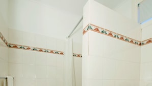 Un baño con paredes de azulejos blancos, zona de ducha e inodoro.