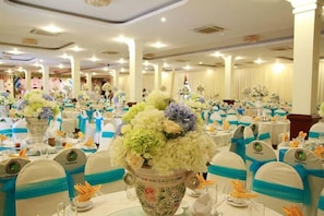 Un salón de banquetes con mesas redondas, sillas adornadas con cintas azules y centros de mesa florales.