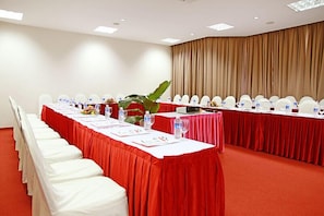 Una sala de conferencias con una larga mesa, sillas blancas y manteles rojos.