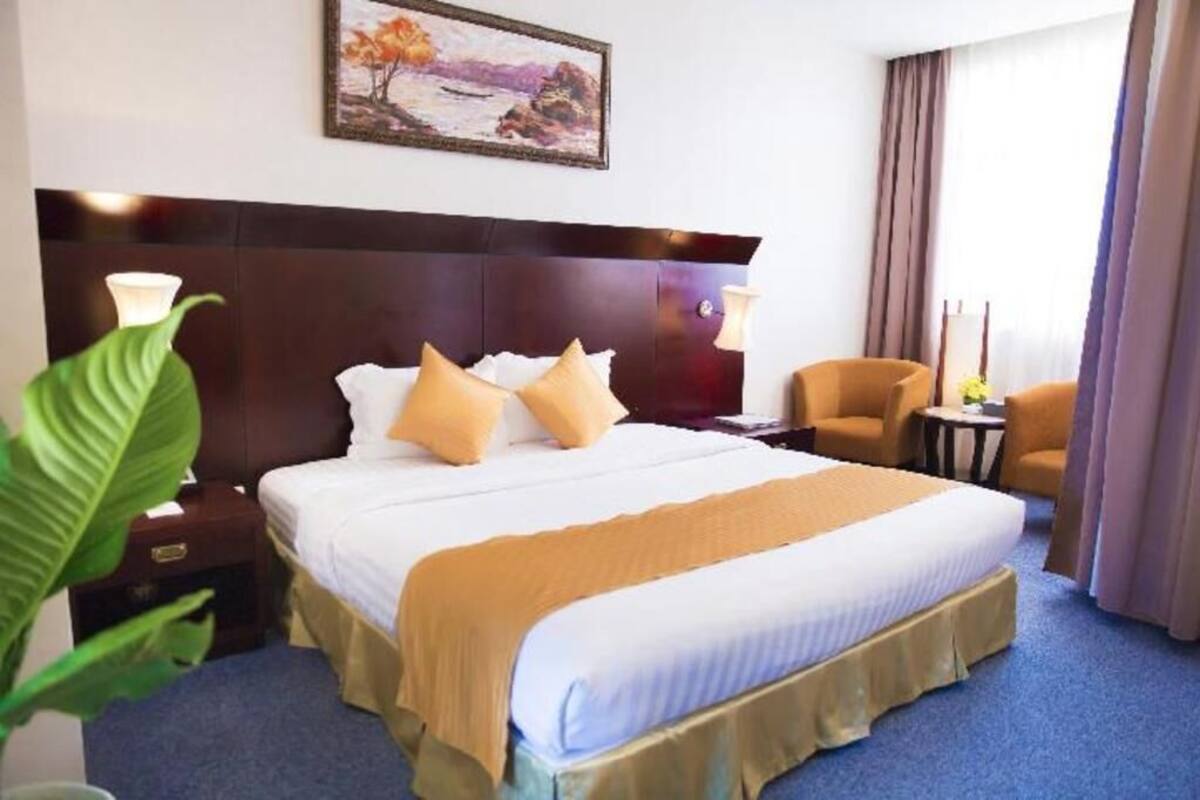 A hotel room with a large bed, two bedside tables, a nightstand, a chair, a small table, and a painting on the wall.