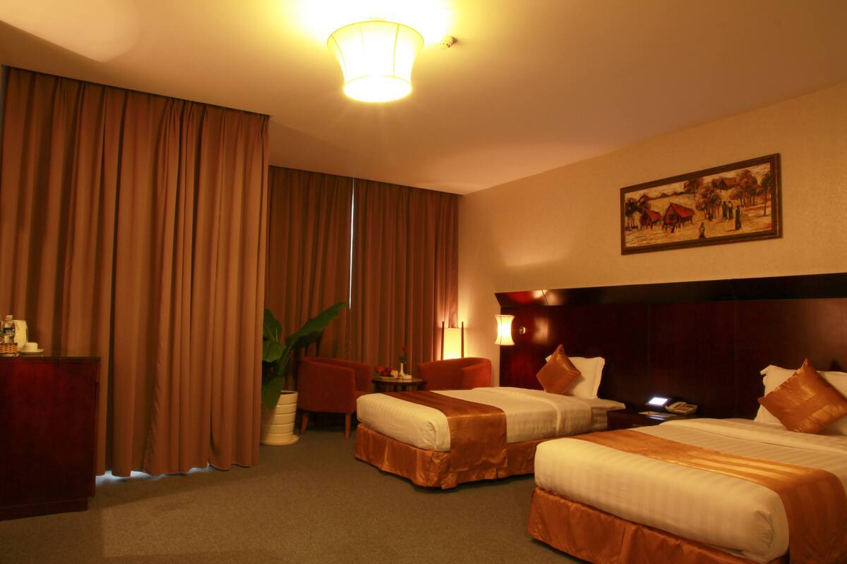 A hotel room with two beds, a desk, a chair, a lamp, and a painting on the wall.