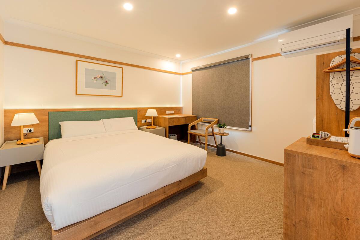 Habitación de hotel con una cama grande, un escritorio con silla, una mesita de noche con lámpara y televisión fijada a la pared.