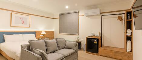A bedroom with a bed, a grey sofa, a small table with a lamp, a wardrobe, and a mirror.