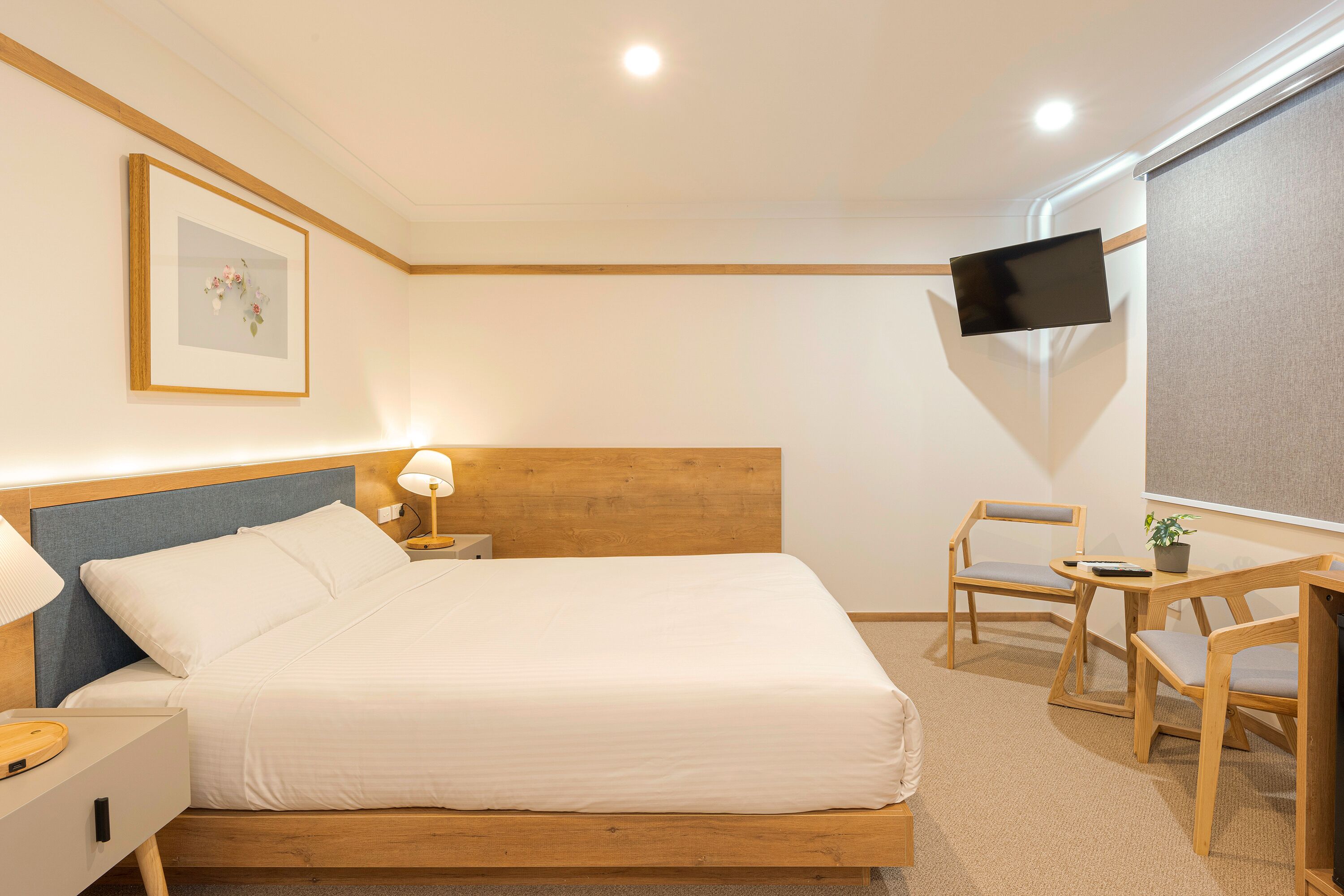 A neatly arranged hotel room with a bed, bedside table, lamp, TV, and seating area.