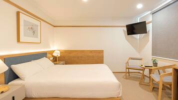 A neatly arranged hotel room with a bed, bedside table, lamp, TV, and seating area.